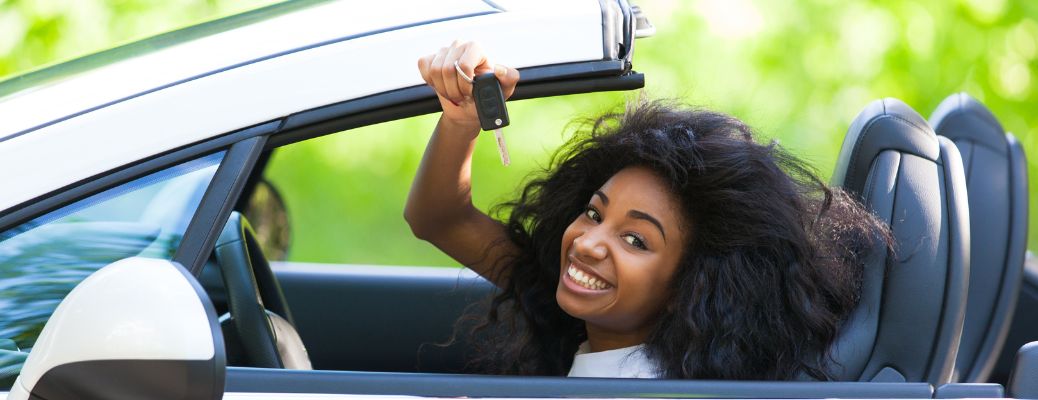 a young girl in driving seat holding out a car key